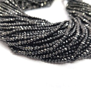 May include: A close-up of a collection of black faceted beads. The beads are strung together, creating a dense, textured appearance. The beads have a reflective quality, catching the light and creating a sparkling effect. The overall theme is jewelry making.