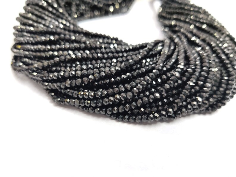 May include: A close-up of a collection of black faceted beads. The beads are strung together, creating a dense, textured appearance. The beads have a reflective quality, catching the light and creating a sparkling effect. The overall theme is jewelry making.