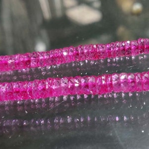 Può includere: Una collana di perle di pietre preziose rosa, probabilmente rubini, infilate su un filo d'argento. Le perle sono sfaccettate e hanno una finitura lucida.