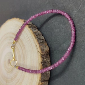 Puede incluir: Un brazalete de piedras preciosas rosas con un cierre de oro. El brazalete está hecho de pequeñas cuentas facetadas.