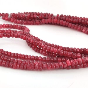 Puede incluir: Una hebra de cuentas de piedras preciosas de color rojo intenso. Las cuentas son pequeñas y redondas, y están enhebradas en un alambre fino. Las cuentas están dispuestas en un patrón suelto y fluido.