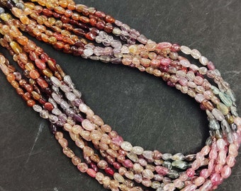 May include: A strand of multi-colored oval-shaped gemstone beads. The beads are a mix of pink, red, orange, and green.