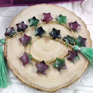 May include: A strand of star-shaped green and pink gemstone beads with gold spacers. The beads are strung on a cord and have tassels on either end.