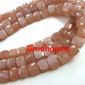 Puede incluir: Una hebra de cuentas de piedra de sol marrón claro, cada cuenta está facetada y tiene una forma cuadrada. Las cuentas están enhebradas en un alambre y están listas para ser utilizadas para la elaboración de joyas.