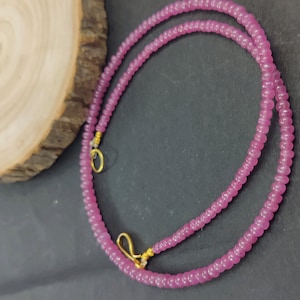 May include: A pink beaded necklace with gold clasps. The necklace is made of small, round beads and is approximately 46 cm long.
