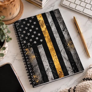 May include: A spiral-bound notebook featuring a distressed American flag design with a black, white, and gold color scheme. The cover displays a field of stars and alternating stripes, with a prominent vertical gold stripe running through the center.