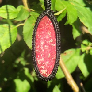 May include: A red gemstone pendant with a black cord necklace. The pendant is oval shaped and has a dark red color with white flecks throughout.