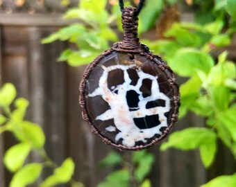 May include: A brown and white agate pendant with a copper wire wrap, hanging from a black cord.