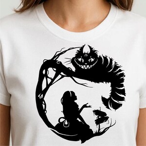 以下が含まれることがあります： 白のTシャツ。黒いシルエットのデザインで、不思議の国のアリスが描かれています。デザインにはアリス、チェシャ猫、物語の舞台の要素が含まれています。グラフィックはシャツの中央に配置されています。