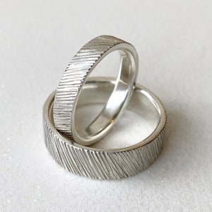May include: Two silver wedding bands with a textured finish. The bands are stacked on top of each other.