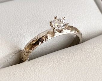 May include: A simple silver band ring with a single, small, round diamond set in a four-prong setting. The band has a hammered texture.