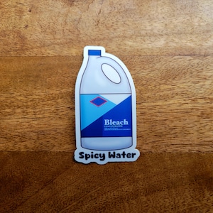 May include: A white plastic bottle with a blue label that says "Bleach Concentrated" and a blue diamond shape. The bottle is on a wooden surface and the text "Spicy Water" is below the bottle.