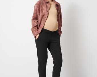 May include: A beige fitted top, a red and black plaid button-down shirt with long sleeves, and black trousers with a cuffed hem. The outfit is completed with white sneakers. The trousers feature a wide, elasticized waistband designed to sit low.