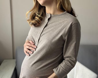 May include: A light brown maternity dress with long sleeves and a button-up front. The dress is made of a soft fabric and is designed for pregnancy. The woman is holding her baby bump.