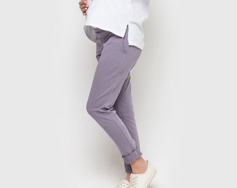 May include: A pair of solid lavender-colored pants with a tapered leg, featuring a high-rise elasticized waistband and cuffed hems, paired with a plain white short-sleeved top and simple white lace-up sneakers for a casual and comfortable look.