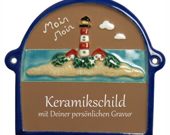 Pode incluir: Um sinal de cerâmica marrom com borda azul, apresentando um farol em uma pequena ilha com arbustos verdes e nuvens brancas. O sinal diz "Moin Moin" e "Keramikschild mit Deiner persönlichen Gravur".