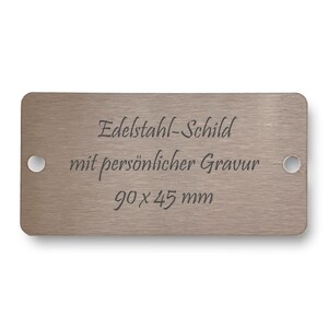 Peut inclure: Une plaque rectangulaire en métal brossé avec des coins arrondis. La plaque porte le texte "Edelstahl-Schild mit persönlicher Gravur" et "90 x 45 mm" en gris foncé. Deux trous sont présents.