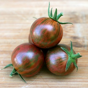 May include: Three small, dark red tomatoes with green stripes. The tomatoes are arranged in a pyramid shape on a wooden surface.