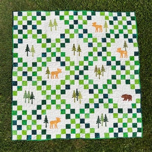 Könnte beinhalten: Eine weiße und grüne Patchwork-Decke mit einem karierten Muster. Die Decke zeigt verschiedene Waldtiere, darunter Elche, Bären und Bäume.