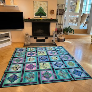 May include: A large quilt with a geometric pattern of squares and diamonds. The quilt is made of fabric with a floral print in shades of green, blue, and purple. The quilt is laid out on a wooden floor.
