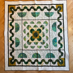 Op de afbeelding: Een wit quilt met een geometrisch patroon in groen en goud. Het patroon bestaat uit cirkels, halve cirkels en vierkanten. Het quilt is afgewerkt met een witte rand.