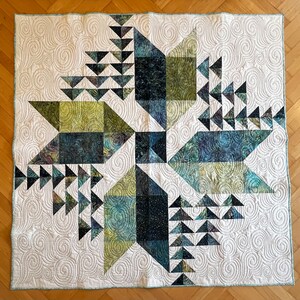 Op de afbeelding: Een wit quilt met een geometrisch ontwerp in tinten groen, blauw en zwart. Het quilt is gemaakt van driehoeken en vierkanten, en het ontwerp is gecentreerd op een stervorm.