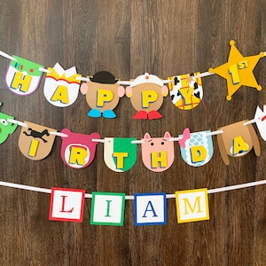 May include: A colorful banner with Toy Story characters and the words "Happy 1st Birthday Liam". The banner is made of paper and has a white string running through it.