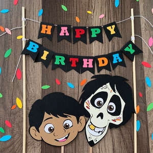 May include: A colourful "Happy Birthday" banner with black pennants and multi-coloured letters. Two character cutouts from the film Coco, Miguel and Hector, are attached to wooden dowels.
