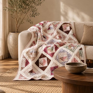 May include: A patchwork quilt featuring a repeating square pattern with various floral prints in shades of pink, purple, brown, and white. The quilt is constructed with white fabric borders separating each square, creating a geometric grid design.