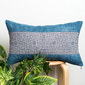 May include: A blue and white patterned cushion with a geometric design. The cushion is sitting on a wooden stool.