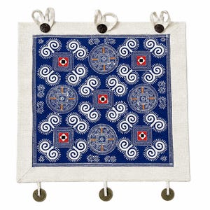 May include: A square textile wall hanging featuring a deep blue center panel with white spiral patterns, geometric squares, and circular motifs. The piece is framed by a light beige border and includes three top loops and three bottom hanging coins.