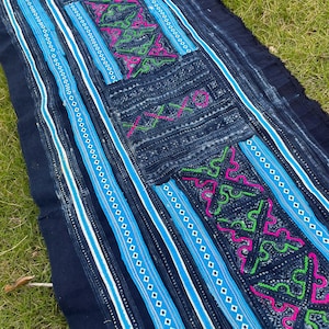 May include: A dark blue fabric with intricate white, blue, green, and pink embroidery. The fabric has a striped pattern and a geometric design.