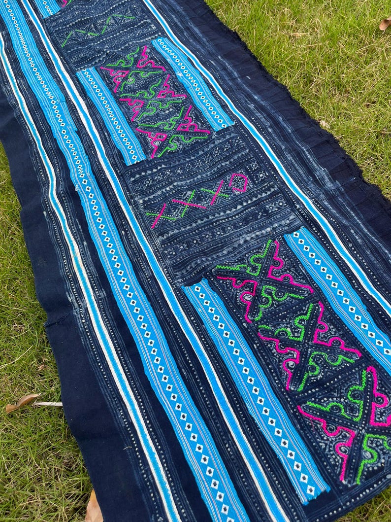 May include: A dark blue fabric with intricate white, blue, green, and pink embroidery. The fabric has a striped pattern and a geometric design.