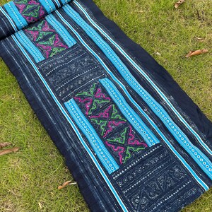 May include: A long piece of indigo-dyed fabric with intricate embroidery in shades of blue, green, and pink. The fabric has a striped pattern and is decorated with geometric designs.
