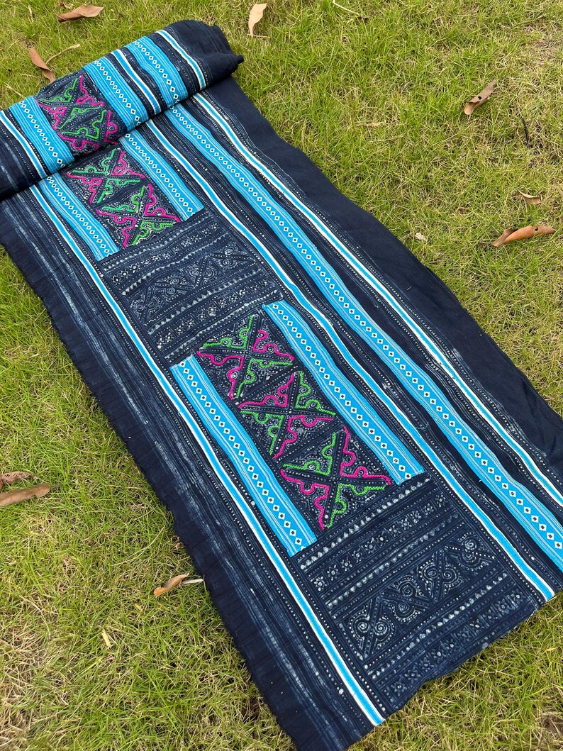May include: A long piece of indigo-dyed fabric with intricate embroidery in shades of blue, green, and pink. The fabric has a striped pattern and is decorated with geometric designs.