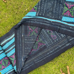 May include: A dark blue indigo fabric with intricate white and blue embroidery. The fabric has a geometric pattern with a repeating design of small squares and diamonds. The fabric is folded in half and the edges are frayed.