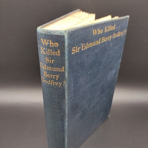 May include: A blue hardcover book with gold lettering on the spine and front cover. The title is "Who Killed Sir Edmund Berry Godfrey?"