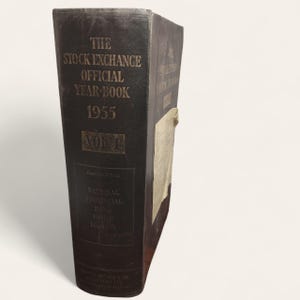 May include: A vintage dark gray "The Stock Exchange Official Year-Book 1955 Vol. 1" book with gold lettering. The book is from the National Provincial Bank Limited, London. The book is in good condition.