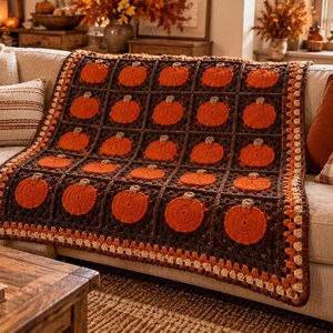 Könnte beinhalten: Eine rechteckige Häkeldecke mit einem sich wiederholenden Muster aus orangefarbenen Kürbismotiven, die in dunkelbraunen Quadraten zentriert sind. Die Decke ist mit einer dekorativen Bordüre aus cremefarbenem, hellbraunem und dunkelbraunem Garn versehen.
