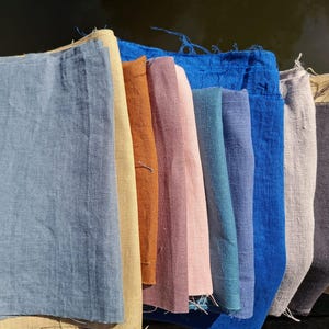 Op de afbeelding: Een verzameling linnen stofstalen in verschillende kleuren, waaronder blauw, beige, roze en grijs. De stalen zijn naast elkaar gerangschikt en tonen de verschillende tinten en texturen van de stof. De afbeelding is goed belicht en benadrukt de natuurlijke vezels.