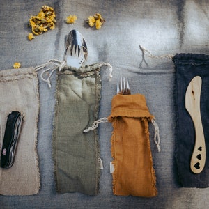 Può includere: Quattro set di posate riutilizzabili in sacchetti di stoffa individuali. I set includono un coltello, una forchetta e un cucchiaio. I sacchetti sono beige, verde, arancio e nero.