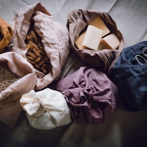 Puede incluir: Una colección de seis bolsas de tela reutilizables llenas de varios artículos, incluyendo pasta, granos y barras de jabón. Las bolsas están hechas de tela natural y son una alternativa sostenible a las bolsas de plástico.