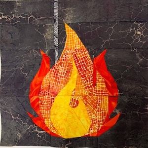 Pode incluir: Um bloco de colcha de retalhos em forma de chama com um design amarelo, laranja e vermelho. O bloco está colocado sobre um fundo cinza escuro com uma textura rachada.