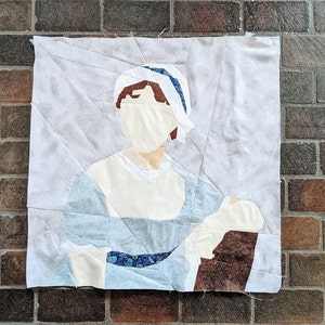 May include: A white and blue patchwork quilt depicting a woman wearing a blue and white dress and a blue and white hat. The quilt is made of various fabrics and textures.