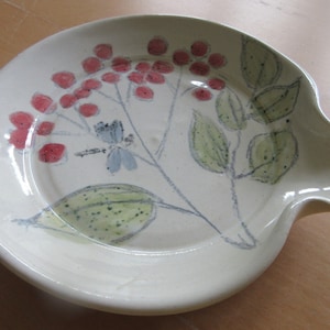 Puede incluir: Un plato de cerámica blanco con un diseño pintado a mano de bayas rojas, hojas verdes y una libélula azul.
