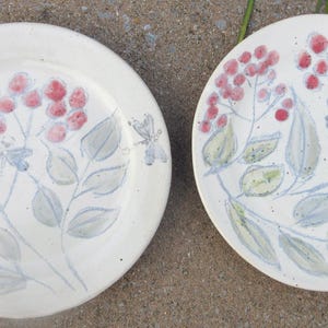 Puede incluir: Dos platos de cerámica blanca con un diseño floral. Los platos presentan una rama de bayas rojas y hojas verdes con un lavado gris claro. Los platos son perfectos para servir postres o aperitivos.