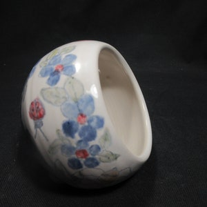 May include: A white ceramic bowl with a floral design. The bowl features blue and red flowers with green leaves.