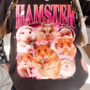 May include: Dark brown t-shirt featuring the word "HAMSTER" in a pink and white gradient font. The shirt displays a collage of hamster images in various poses. The model is wearing a black and white checkered long sleeve shirt underneath.