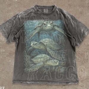 A t-shirt with a graphic design depicting three sea turtles swimming in the ocean.