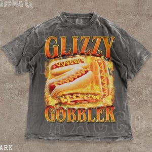 A grey t-shirt with a graphic design featuring two hot dogs on a flame background, along with the text "GLIZZY GOBBLER" prominently displayed.